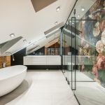 bagno in legno chiaro, con vasca da bagno bianca, doccia in vetro e calorifero nero.